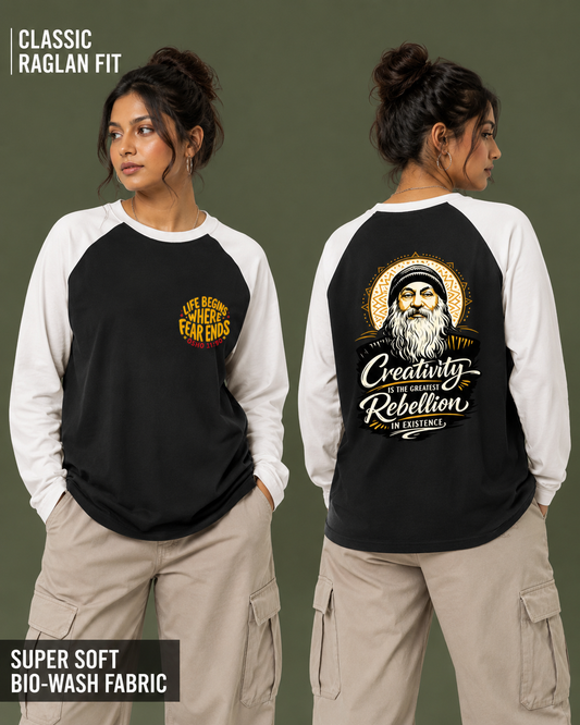 A woman modeling a black and white raglan long-sleeve shirt, shown from both front and back against a muted olive background. The front has a small yellow graphic on the left chest, and the back has a large graphic with a bearded figure and the words 'Creativity is Rebellion' and 'Live Your Best Fearless Life.
